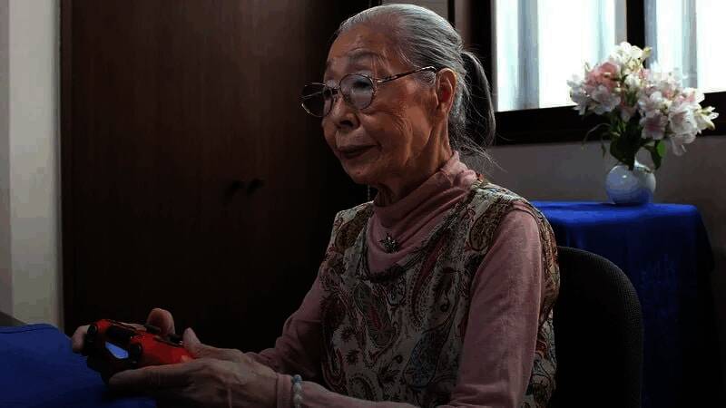 Will爷爷坐在家中游戏室,面对多块显示屏进行直播,手边摆放着特制防麻木键盘,背景墙上贴满粉丝寄来的支持信件