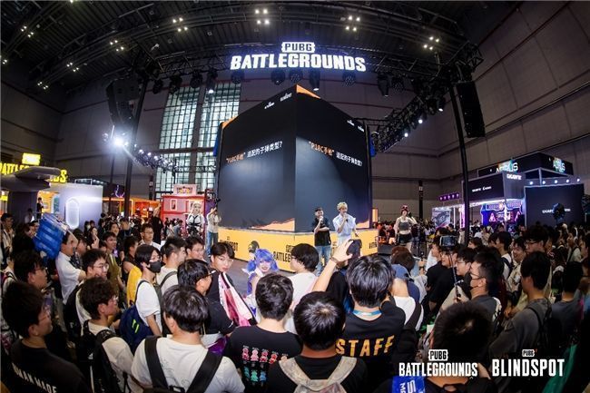 职业选手GODV在舞台上展示白色联名外套，台下观众举手机拍摄