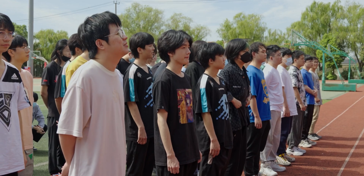 OPL练就营开营仪式现场全景，多支战队选手身着统一运动服整齐列队，背景悬挂‘锋芒所向，竞逐未来’主题横幅，气氛庄重而充满朝气