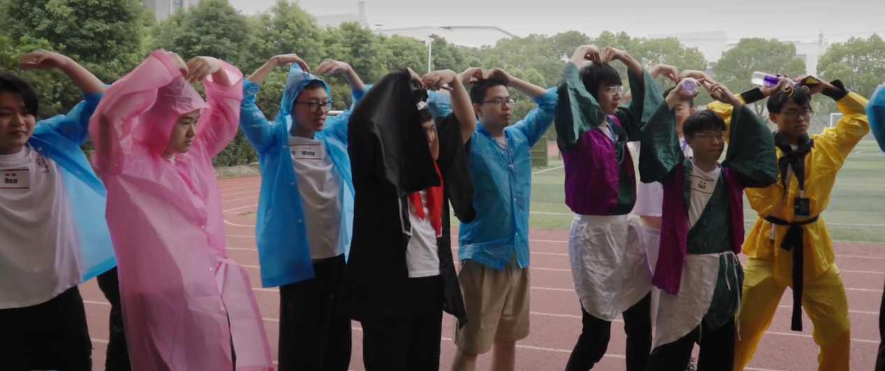 夜晚教室内部场景：十余名选手坐姿端正，专注观看投影幕布上的赛事规则动画演示，桌上摆放笔记本与荧光笔，氛围安静而求知欲浓厚