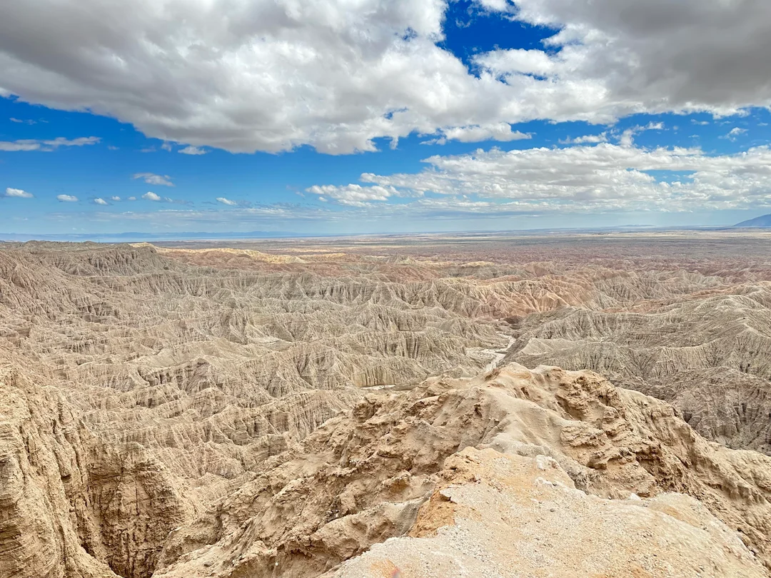Anza-Borrego沙漠日落场景：低角度阳光将长条形砂岩投下锐利阴影，地面泛起金属质感的暖金色反光，远处地平线处有微弱大气辉光